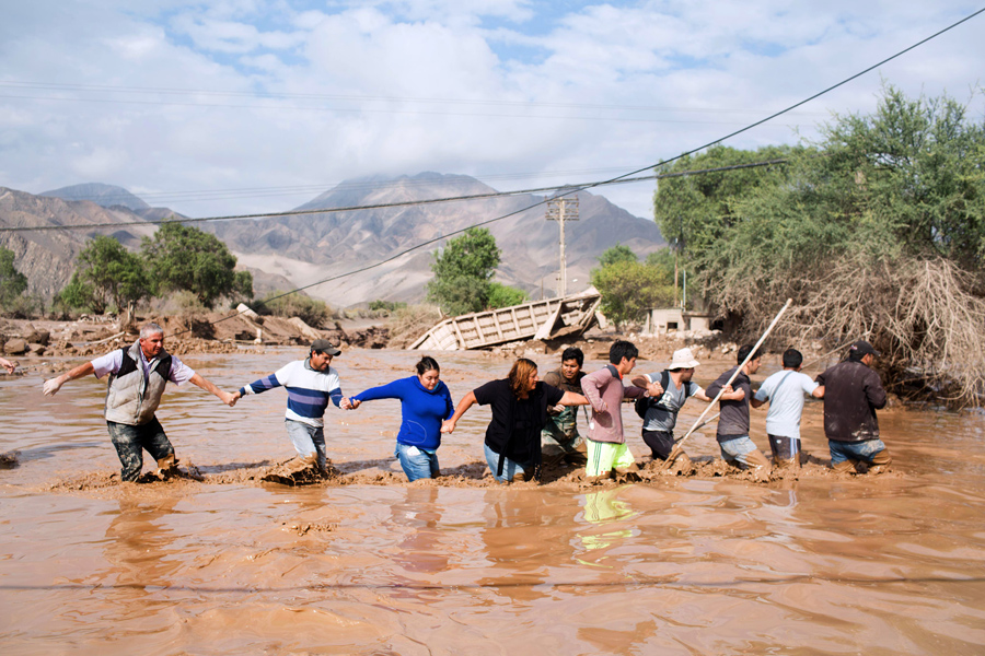 Местные жители переходят дорогу затопленную проливными дождями недалеко от города Копьяпо, Чили.