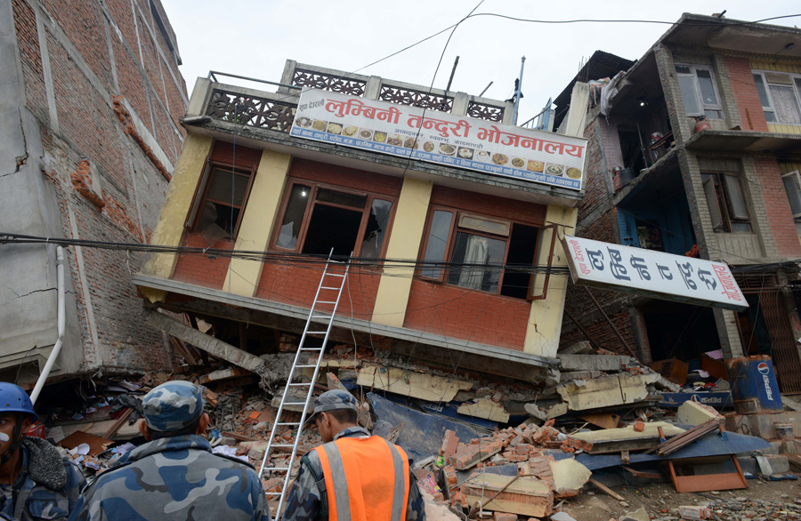 Непальские спасатели наблюдают за поврежденным зданием после землетрясения в Катманду.