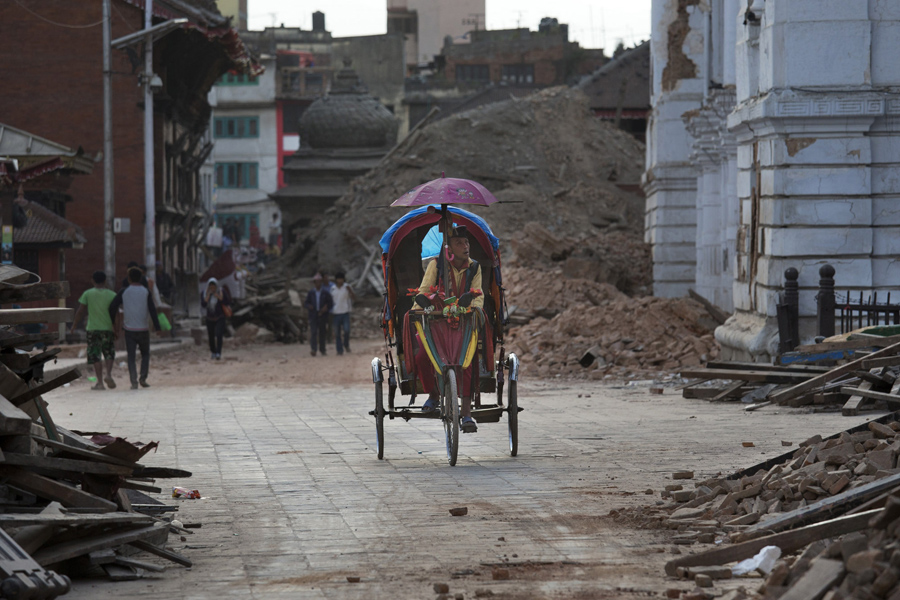 Мужчина крутит педали, проезжая мимо поврежденных зданий на площади Дурбар в Катманду.