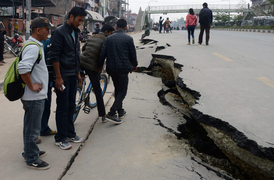 Непальские жители проходят мимо поврежденного дорожного полотна после землетрясения в Катманду.