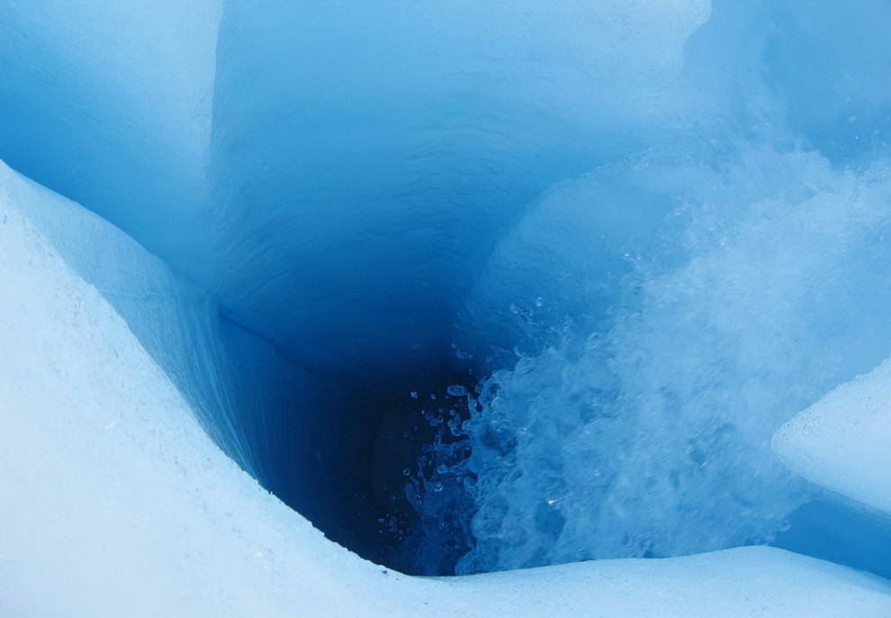 Water flowing into a small "moulin" roughly 3 feet wide. This feature probably does not extend directly to the ice-sheet base. Instead, it like flows laterally through a crack at some depth to connect with a large moulin that does reach the bed.