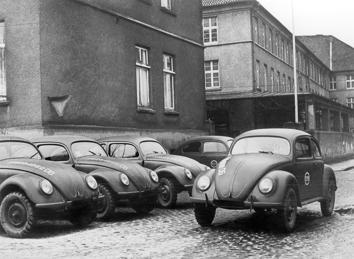 In 1945 the first Volkswagens made in West Germany, at Bonneberg near Kerford, are parked in the factory's courtyard. The Beetle owes its existence to Adolf HITLER's will to equip the IIIrd Reich with a popular car. It became commercialized only in the post-war period and is a symbol of those years. En 1945, les premières Volkswagen fabriquées en Allemagne de l'Ouest, à Bonneberg, près de Kerford sont stationnées dans la cour de l'usine. La Coccinelle doit son existence à la volonté d'Adolf HITLER de doter le IIIe Reich d'une voiture populaire. Elle n'est commercialisée qu'après-guerre et constitue un symbole de ces années-là.