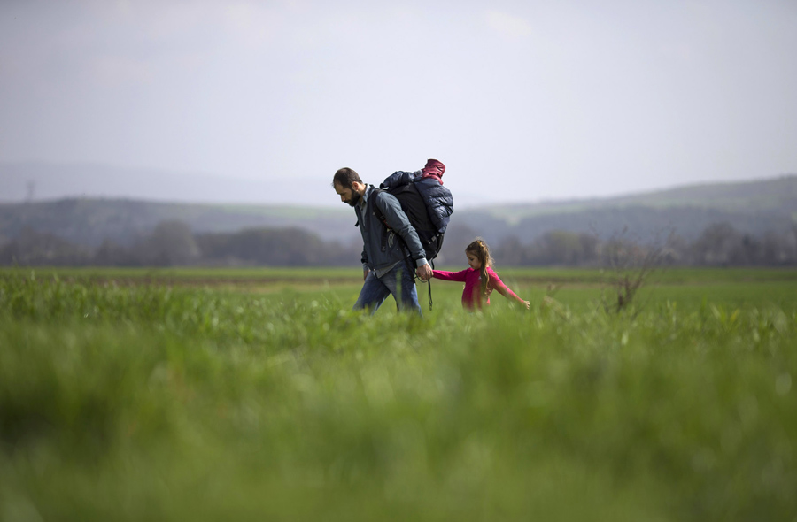 Мужчина держит за руку девочку и идут по полю к македонской границе.