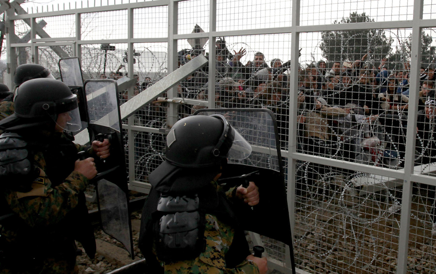 Беженцы и мигранты пытаются сломать забор на границе, македонские полицейские используют свои щиты для сдерживания, возле македонского города Гевгелия 29 февраля 2016 года.