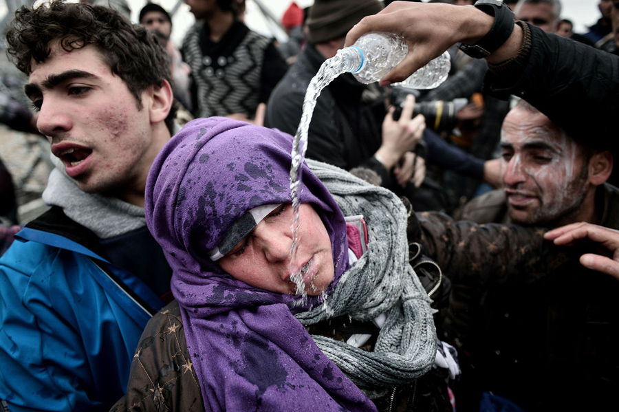 Беженец льет воду на лицо женщины, которая потеряла сознание после того как потеряла ребенка в панической толпе. Македонская полиция применила слезоточивый газ против беженцев в греко-македонской границе 29 февраля 2016 года.