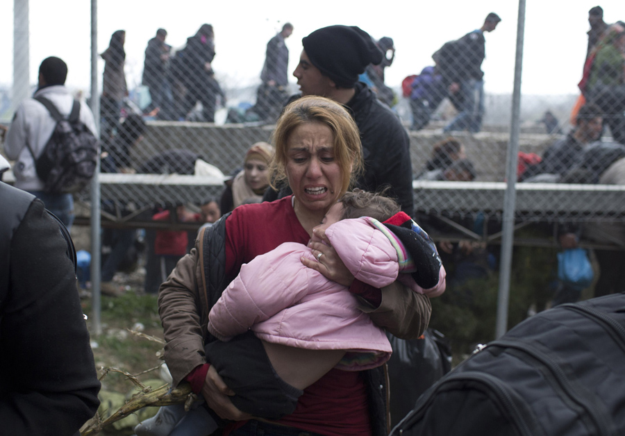Женщина несет ребенка на греческой стороне границы, она убегает после того как македонская полиция применила слезоточивый газ, 29 февраля 2016 года.