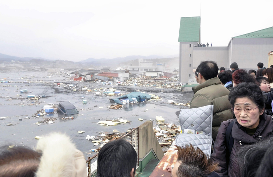 Люди смотрят на последствия цунами после землетрясения в городе Кесеннума, префектура Мияги, 11 марта 2011 года.