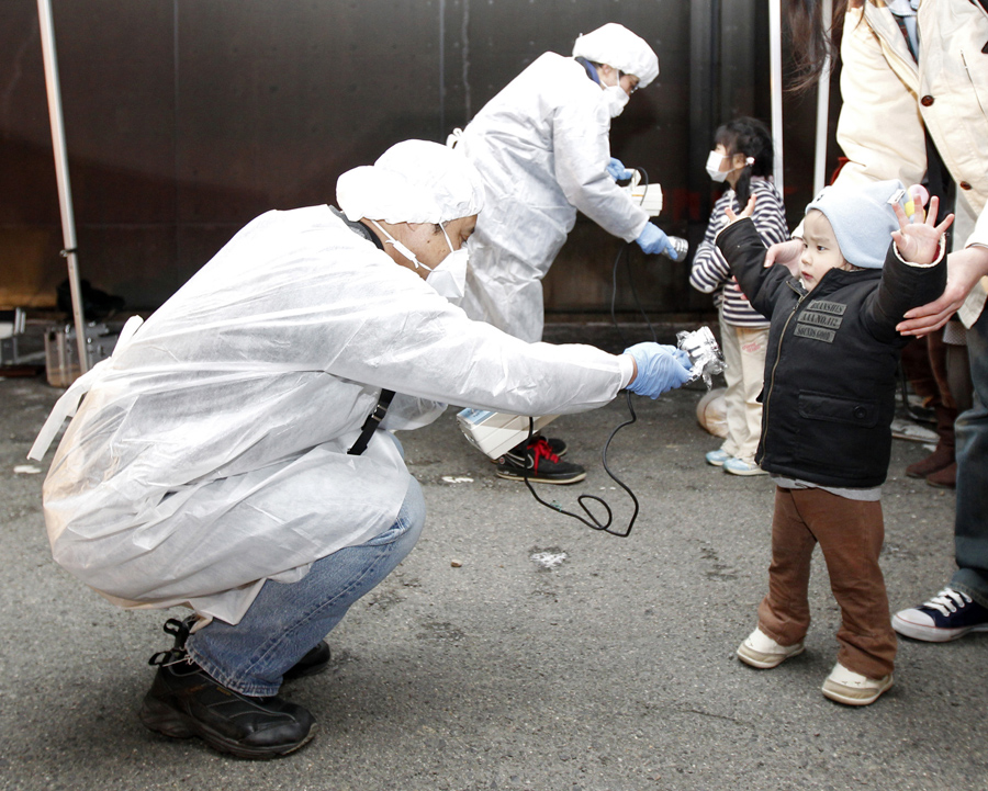 Люди в защитных снаряжения проверяют детей на признаки радиации в эвакуационной зоне рядом с Фукусимой, 13 марта 2011.
