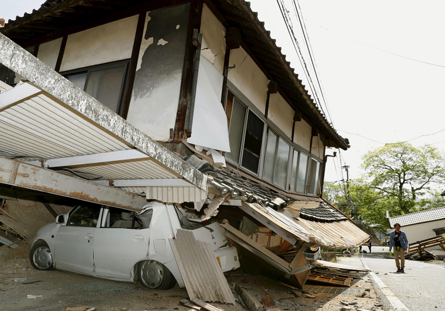Мужчина проходит возле дома который рухнул на автомобиль в результате землетрясения, 15 апреля 2016 года.