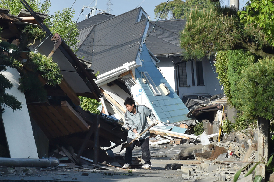 Мужчина убирает мусор у разрушенного дома в Машику, префектура Кумамото, 16 апреля 2016 года.
