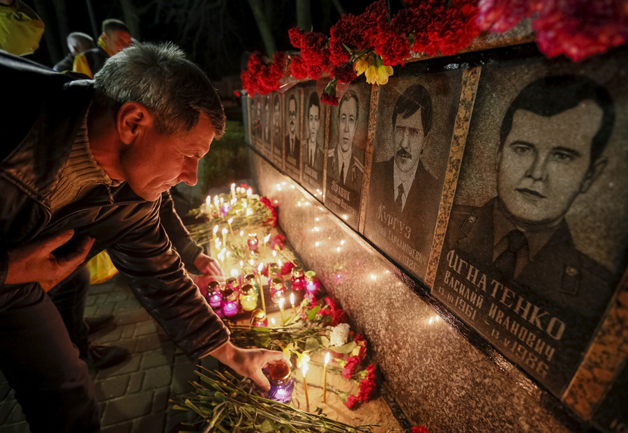 Мужчина зажигает свечи у мемориала посвященного пожарным и работникам станции, которые погибли после катастрофы на Чернобыльской АЭС во время ночной службы, 25 апреля 2015 года.