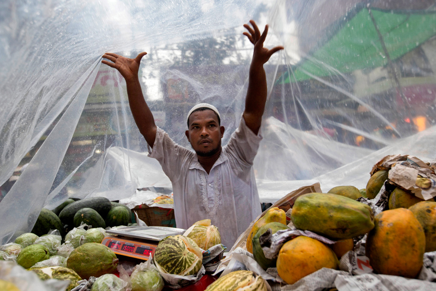 Придорожный продавец фруктов в Бангладеше покрывает свой прилавок прозрачной плёнкой в Дакке, Бангладеш, 7 июня 2016 года.