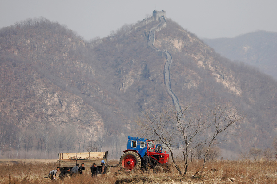 Северокорейские фермеры работают в поле, видна часть Великой стены на китайской стороне реки Ял, к северу от города Синыйджу в Северной Корее, 2 апреля, 2017.