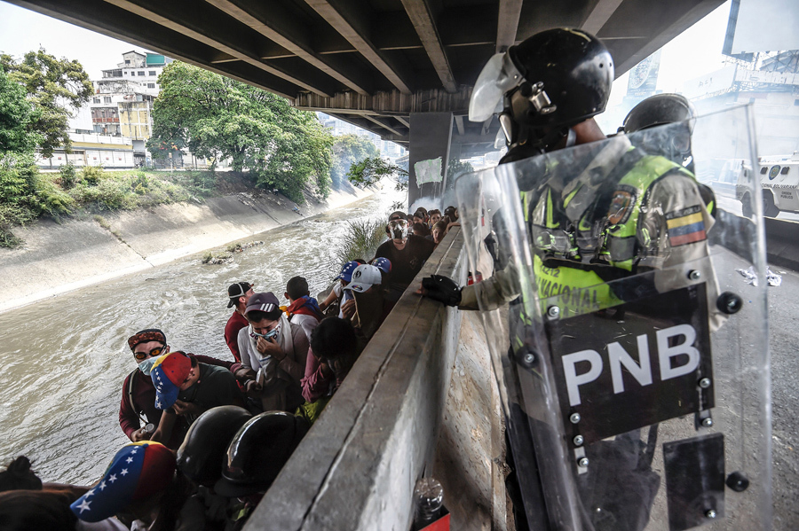 Полиция следит за демонстрантами после столкновений во время митинга против президента Венесуэлы Николаса Мадуро, Каракас, 19 апреля, 2017.