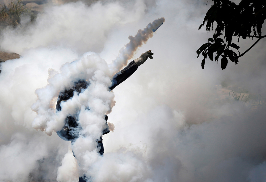 Демонстратор откидывает гранату со слезоточивым газом во время столкновения с полицией в Каракасе 19 апреля 2017 г.