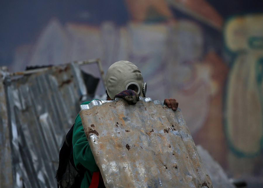 Оппозиционер укрывается металлическим листом во время столкновения с полицией в Каракасе 19 апреля 2017.