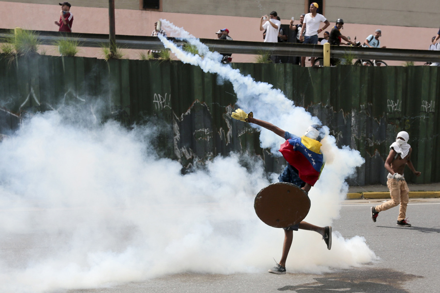 Протестующий откидывает гранату со слезоточивым газом во время антиправительственных протестов в Каракасе 19 апреля 2017. 