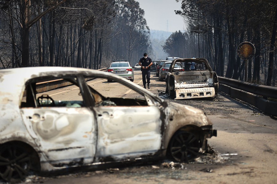 Полицейский ходит по дороге мимо сгоревших автомобилей после лесного пожара в Figueiro dos Vinhos, 18 июня 2017.