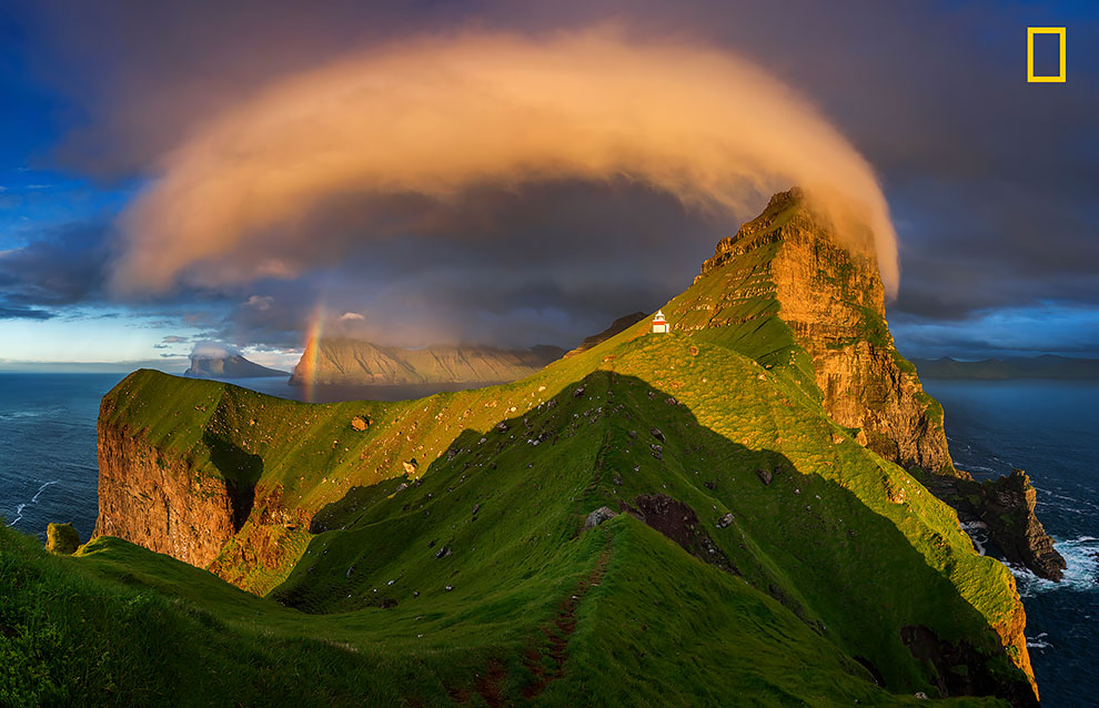 Закат освещает маяк и радугу на Фарерских островах.
